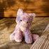 GUND Cozys Kitten plush toy in pastel purple polyester fur with a fuzzy surface and relaxed seated form, displayed on a textured rug indoors to highlight cozy décor appeal and everyday playtime companionship.
