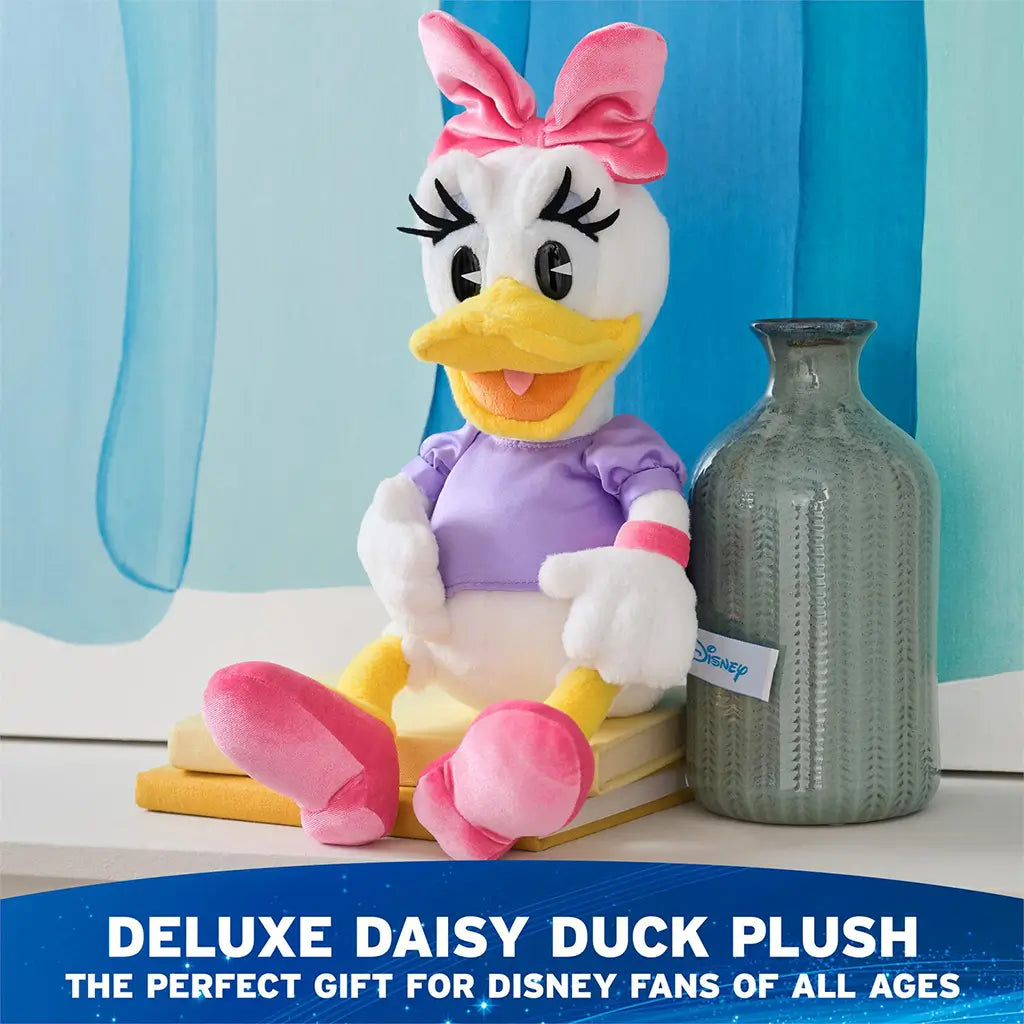 Disney Daisy Duck plush toy displayed seated on books beside a ceramic vase, featuring white plush fabric, yellow beak, pink bow and shoes, lavender satin shirt, and classic character styling in a bright room setting.
