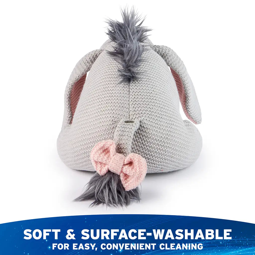 Disney Eeyore knit plush is shown from the back, highlighting gray knit fabric, fluffy mane, stitched tail with pink bow accent, and soft surface-washable design for easy care.