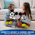 Disney Minnie Mouse plush toy in black and white soft fabric with classic seated character form, red hat with yellow flower, blue polka dot skirt, white gloves, and yellow shoes, displayed with another Minnie and Mickey plush as collectible décor.