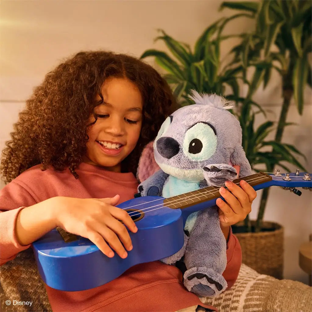 Disney Stitch plush toy with pastel blue plush texture and floppy ears, designed as a comforting companion, held while a child plays a small blue ukulele in a cozy living room setting.