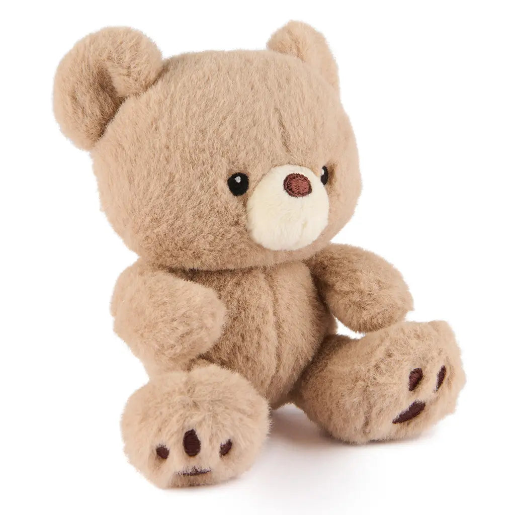 GUND Kai plush teddy bear in light beige fluffy fabric with rounded ears and soft body, angled seated pose showing textured fur and stitched details, small toy on a white background
