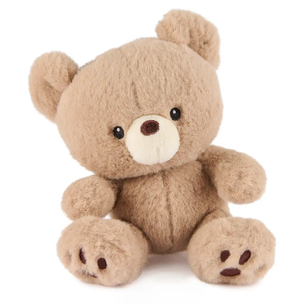 GUND Kai plush teddy bear in light beige soft fabric with rounded body and plush texture, slightly tilted pose emphasizing cuddly form and stitched features, small toy on white background