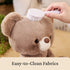 GUND teddy bear easy-clean feature image showing warm beige plush fur, ultra-soft textured fabric, rounded bear head, being gently brushed with a white handheld brush to highlight washable, easy-care materials for everyday use.