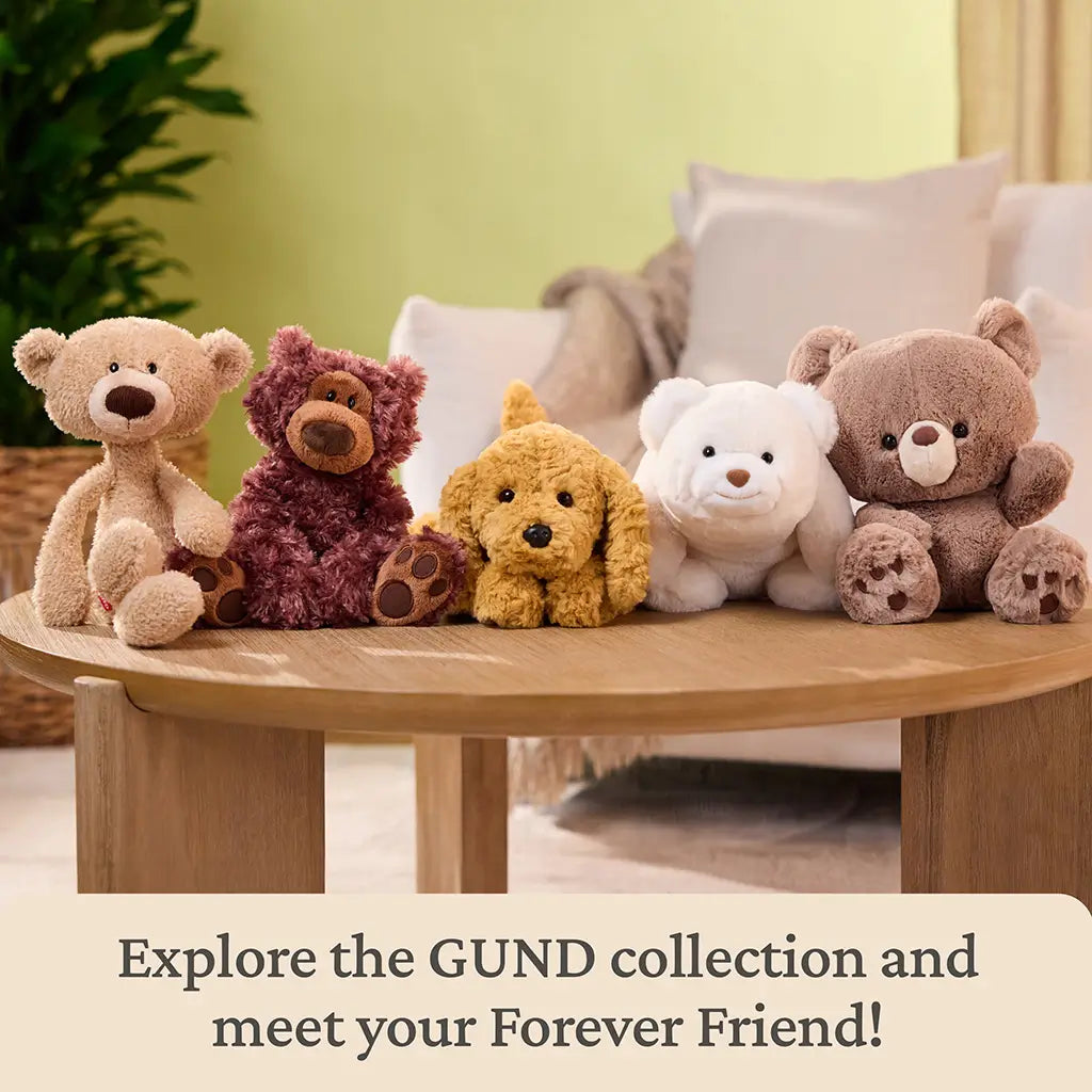 GUND plush collection display showing neutral-toned teddy bears and a puppy made of soft, textured plush fabric, sitting upright on a round wooden table in a cozy living room setting, inviting exploration of the GUND collection.
