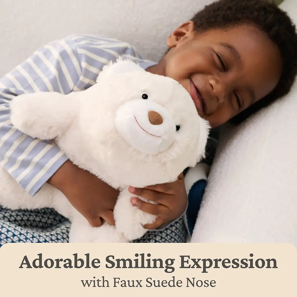 GUND Snuffles teddy bear plush in creamy white polyester fabric with a rounded squishy body, hugged closely by a smiling child on a bed, highlighting emotional comfort, softness, and bedtime companionship.
