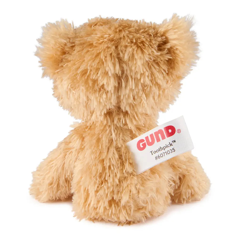 GUND Toothpick plush teddy bear in light tan shaggy fabric with rounded ears and compact shape, rear view showing stitched tag detail, small cuddly toy displayed on a clean white background