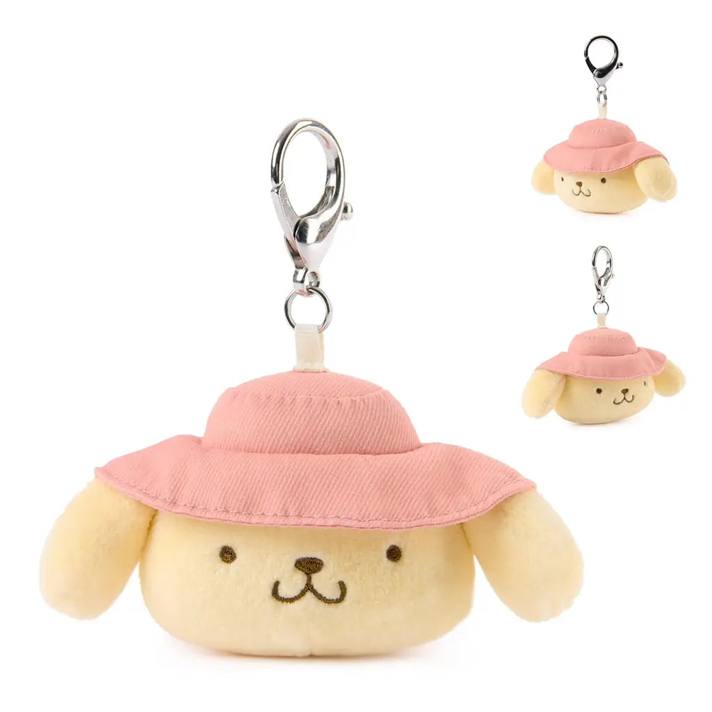 Pompompurin plush keychain from GUND in warm yellow velour fabric with smooth texture, rounded puppy face, embroidered eyes and smile, pink camping hat, and silver clip, designed as a portable 3.5 inch surprise plush.