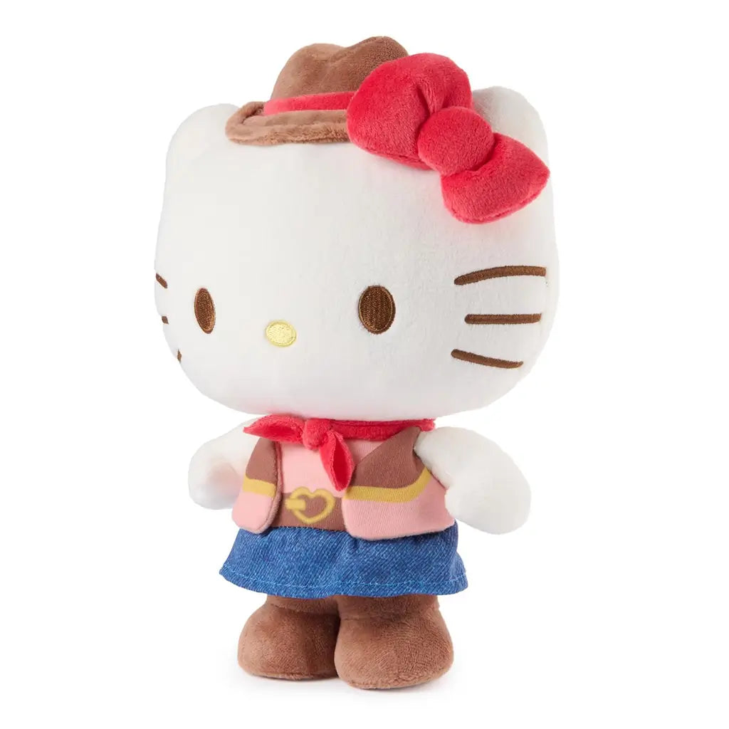 Hello Kitty cowgirl plush by GUND shown at an angled view in white velour fabric with rounded body form, embroidered facial details, brown cowboy hat, red bow, pink vest, blue skirt, and brown boots on a clean white studio background.