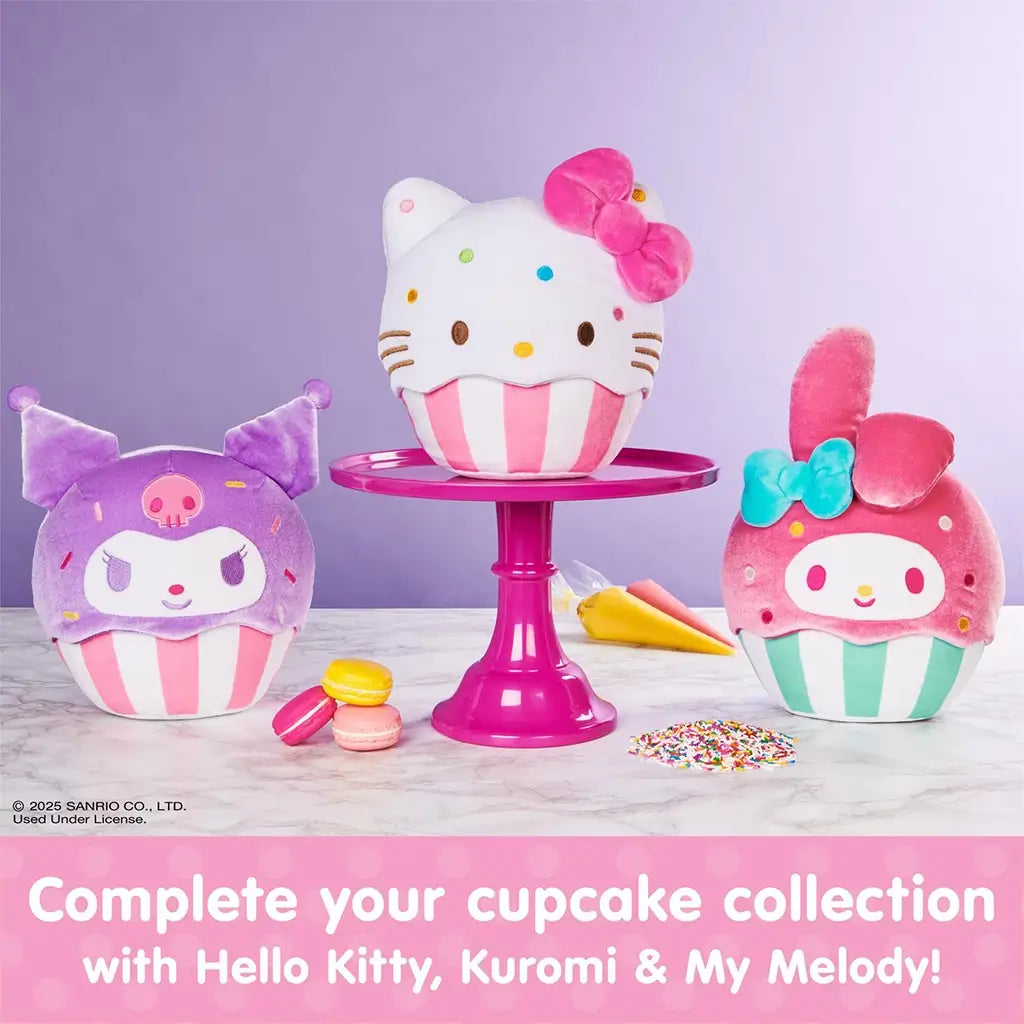 GUND Hello Kitty cupcake plush displayed with Kuromi and My Melody cupcake plush in soft velour fabric, rounded dessert shapes, pastel pink and purple colors, striped cupcake bases, and embroidered details, arranged on a cake stand and marble surface.