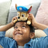 Paw Patrol Chase plush toy in brown and tan soft fabric with blue police hat, small rounded dog shape placed playfully on child’s head in bright indoor living room setting