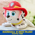 Paw Patrol Marshall plush toy in white and black spotted soft fabric with red firefighter hat, small rounded dog shape posed lying forward on couch in bright indoor living room