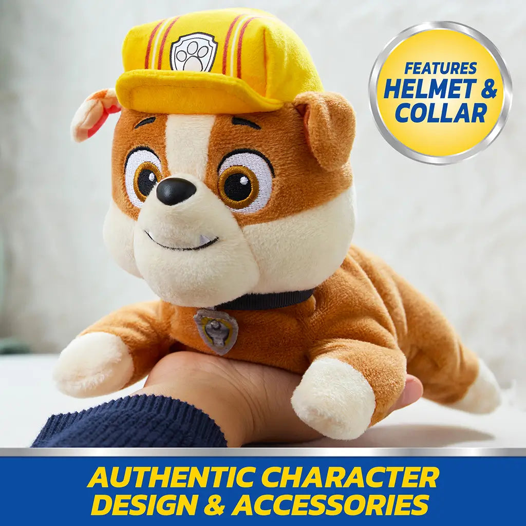 Paw Patrol Rubble plush toy in tan, cream, and yellow soft fabric with helmet and collar, rounded bulldog form designed for imaginative play, displayed on child’s hand indoors