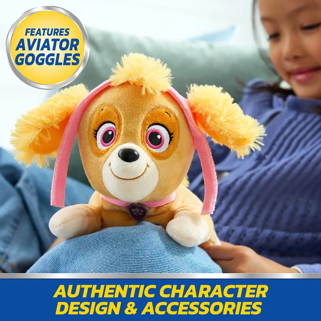 Paw Patrol Skye plush toy in tan and pink soft fabric with aviator goggles and floppy ears, rounded dog form designed for imaginative play, placed on child’s lap in living room