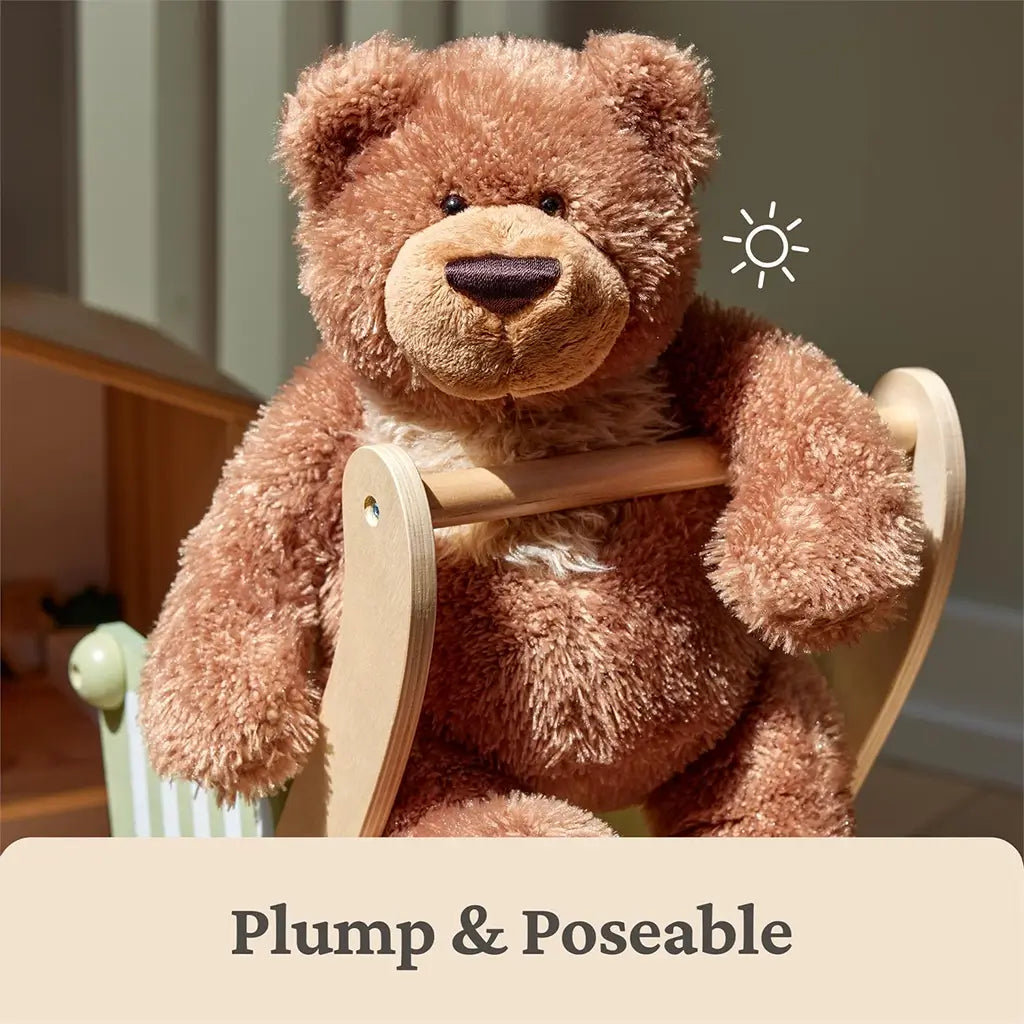 GUND Slumbers teddy bear plush in medium brown fuzzy fabric with plump poseable body, rounded seated bear form, embroidered nose and paw pads, displayed sitting on a wooden toy chair in a softly lit indoor setting.
