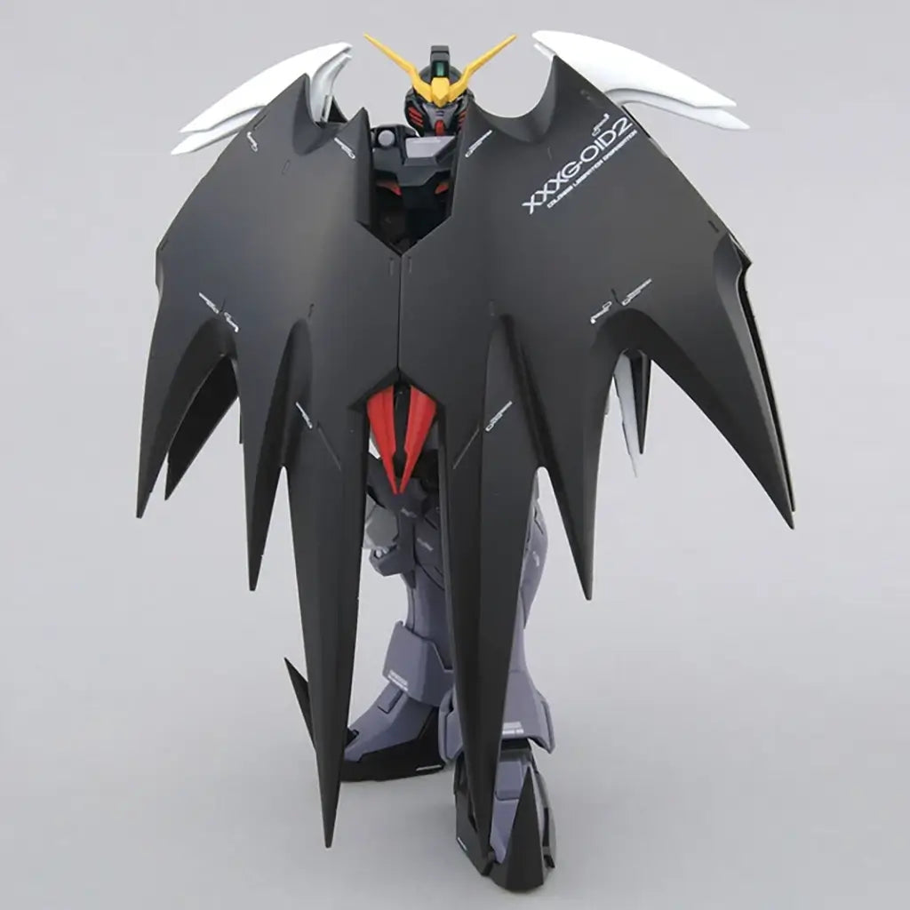Bandai Gundam Deathscythe Hell articulation view in black matte plastic armor with white and red details, closed cloak-like wings forming a spiked silhouette, standing upright on a base in a neutral white studio.