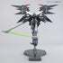 Bandai Gundam Deathscythe Hell front view in black and gray plastic with red chest vents and yellow V-fin, large batlike wings extended, gripping a green beam scythe while mounted on a stand against white background.