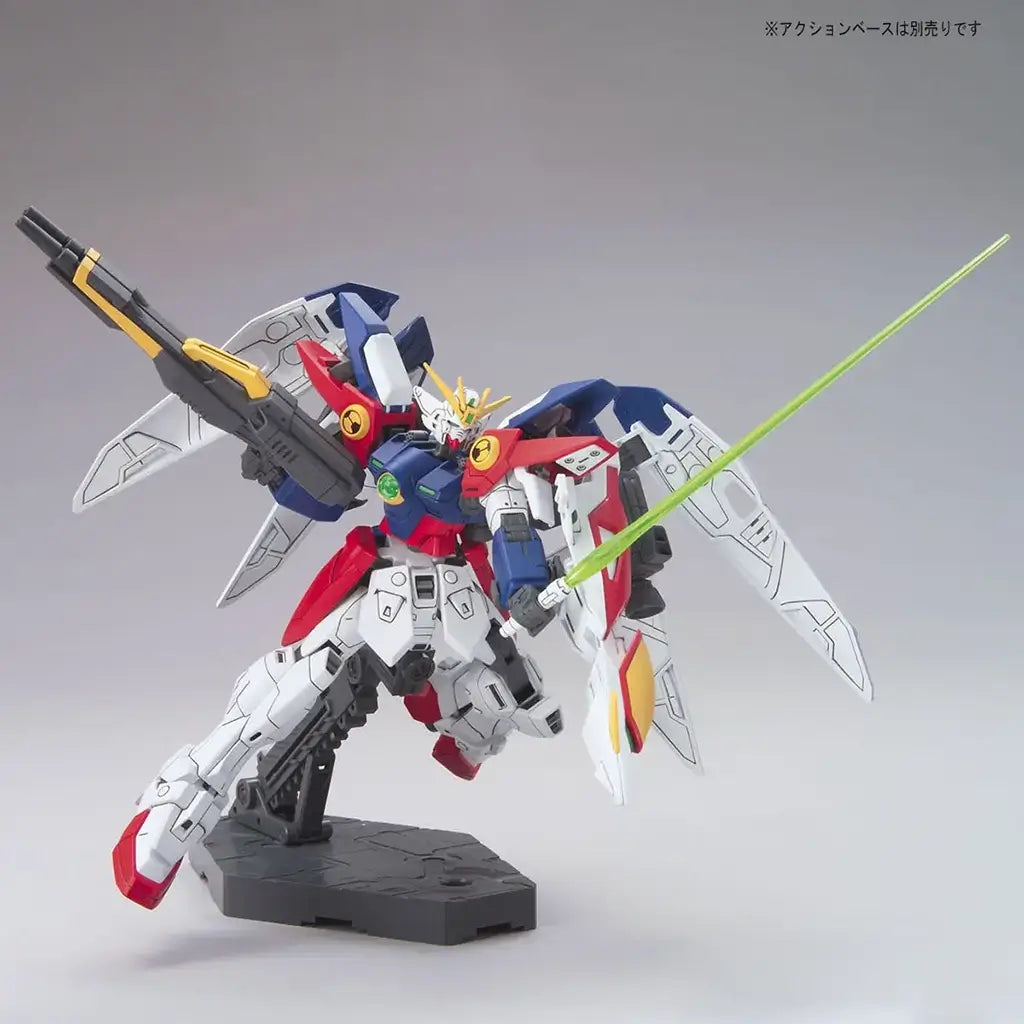 Bandai Wing Gundam Zero model kit in white, blue, and red plastic with humanoid form, featuring beam saber and rifle accessories, articulated mecha posed in action stance on a display base against neutral background