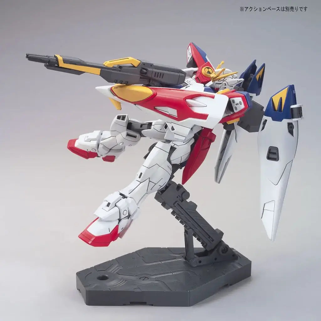 Bandai Wing Gundam Zero model kit in white, blue, red, and yellow plastic with humanoid armored form, featuring extended wings and rifle weapon, poseable mecha figure displayed on a stand against neutral background
