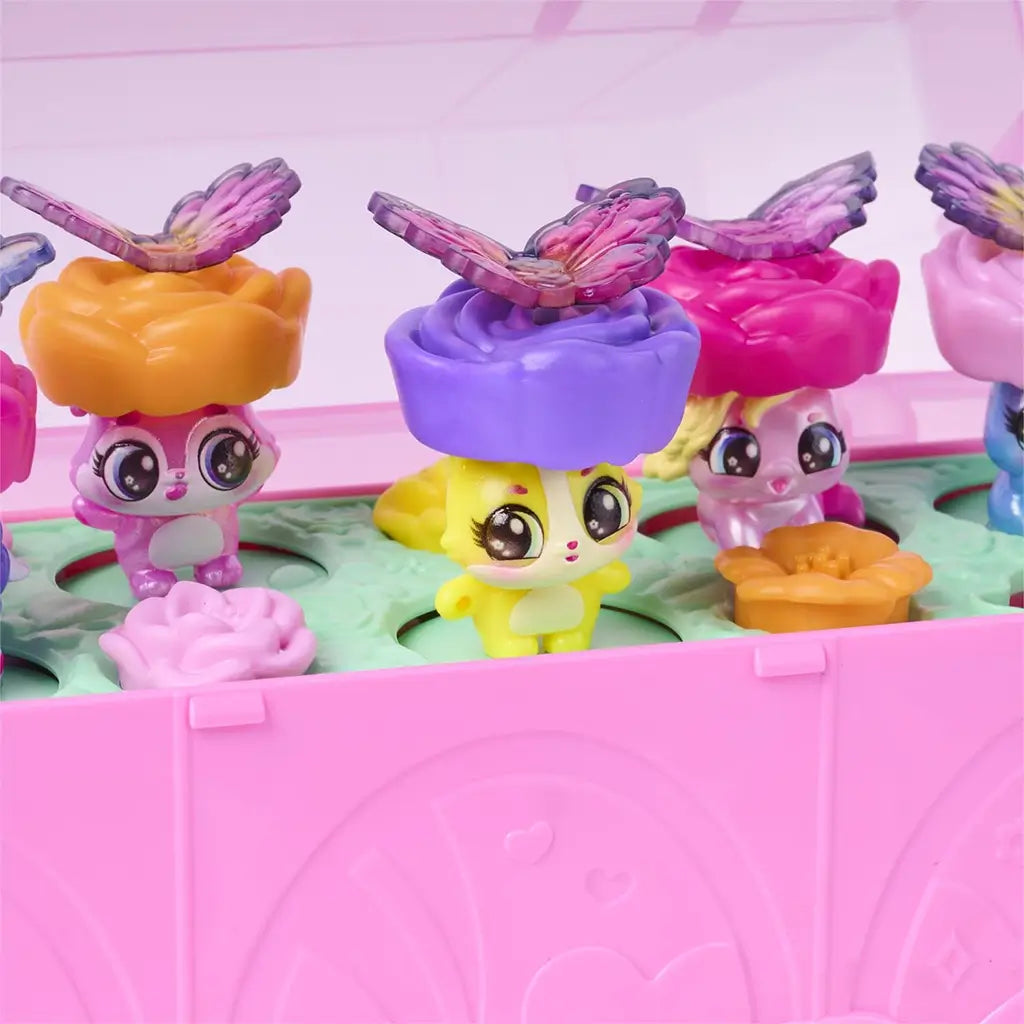 Hatchimals Bloomables close-up highlighting translucent butterfly wings, layered flower accessories, and smooth plastic textures as figures pop up from molded green tray inside the pink terrarium playset.