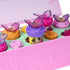 Hatchimals Bloomables close-up view of pastel figures emerging from flower bases inside the terrarium, showing glossy plastic finish, detailed wings, expressive faces, and interactive pop-up play mechanism.