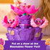 Hatchimals Bloomables Flower Fest stage playset with three characters seated in bright pink flower petals on a purple platform, showing molded details, wing slots, and decorative heart and floral accents.