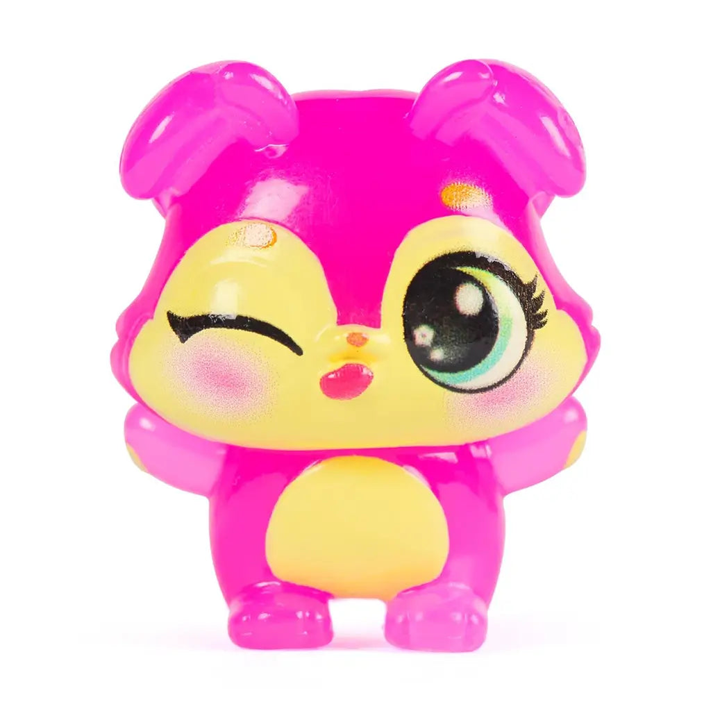 Hatchimals Bloomables collectible character close-up showing glossy translucent pink plastic mini figure with yellow face, winking eye, rounded ears, and smooth molded body posed against a white background.