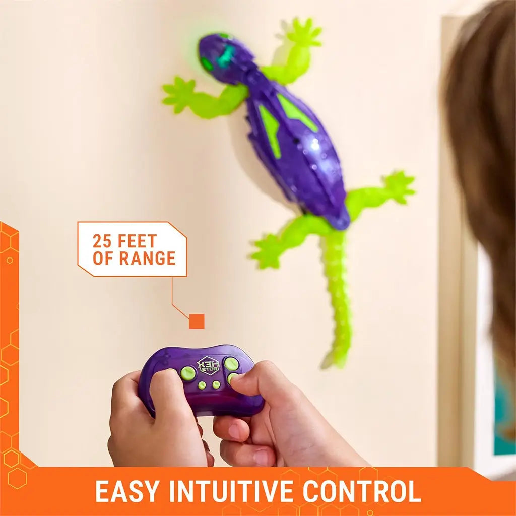 HEX BOTS Wall Crawler gecko in purple and neon green molded plastic with glowing limbs and long tail, shown climbing a wall as hands hold the matching remote with 25 feet range callout.