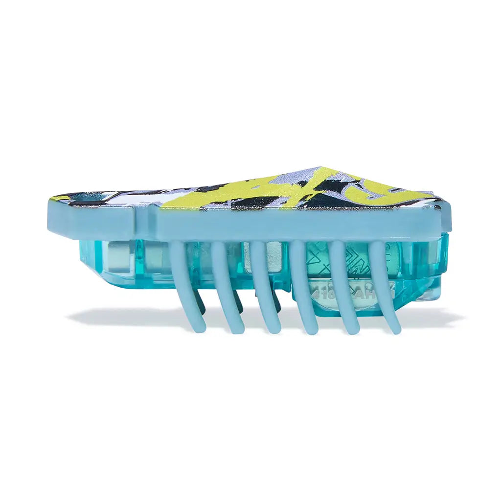HEXBUG Nano robot bug side view in green camo plastic with translucent teal base, low rectangular body and evenly spaced rubber legs, designed for quick vibrating motion on a clean white background.