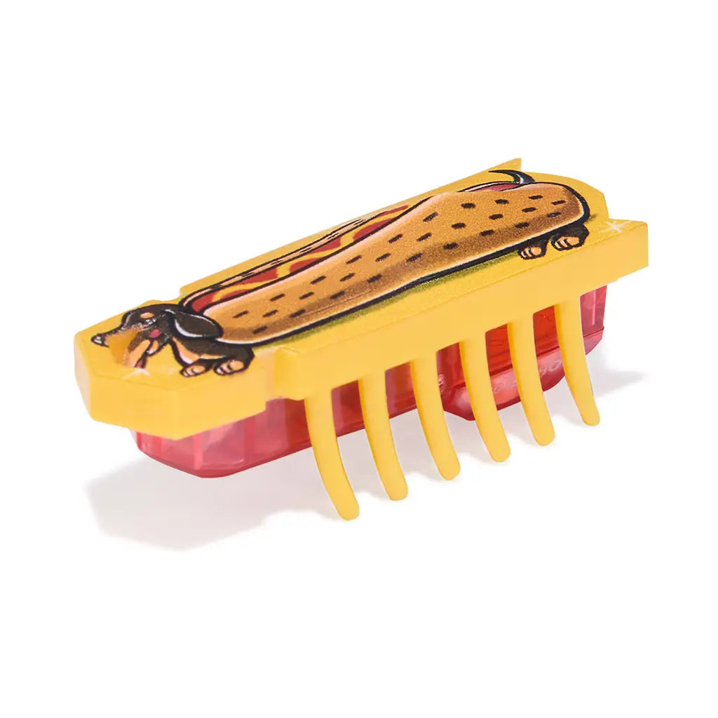 HEXBUG Nano robot bug angled view in yellow plastic with detailed hotdog graphic, low-profile rectangular body and flexible legs, designed for interactive vibrating play on a white backdrop.