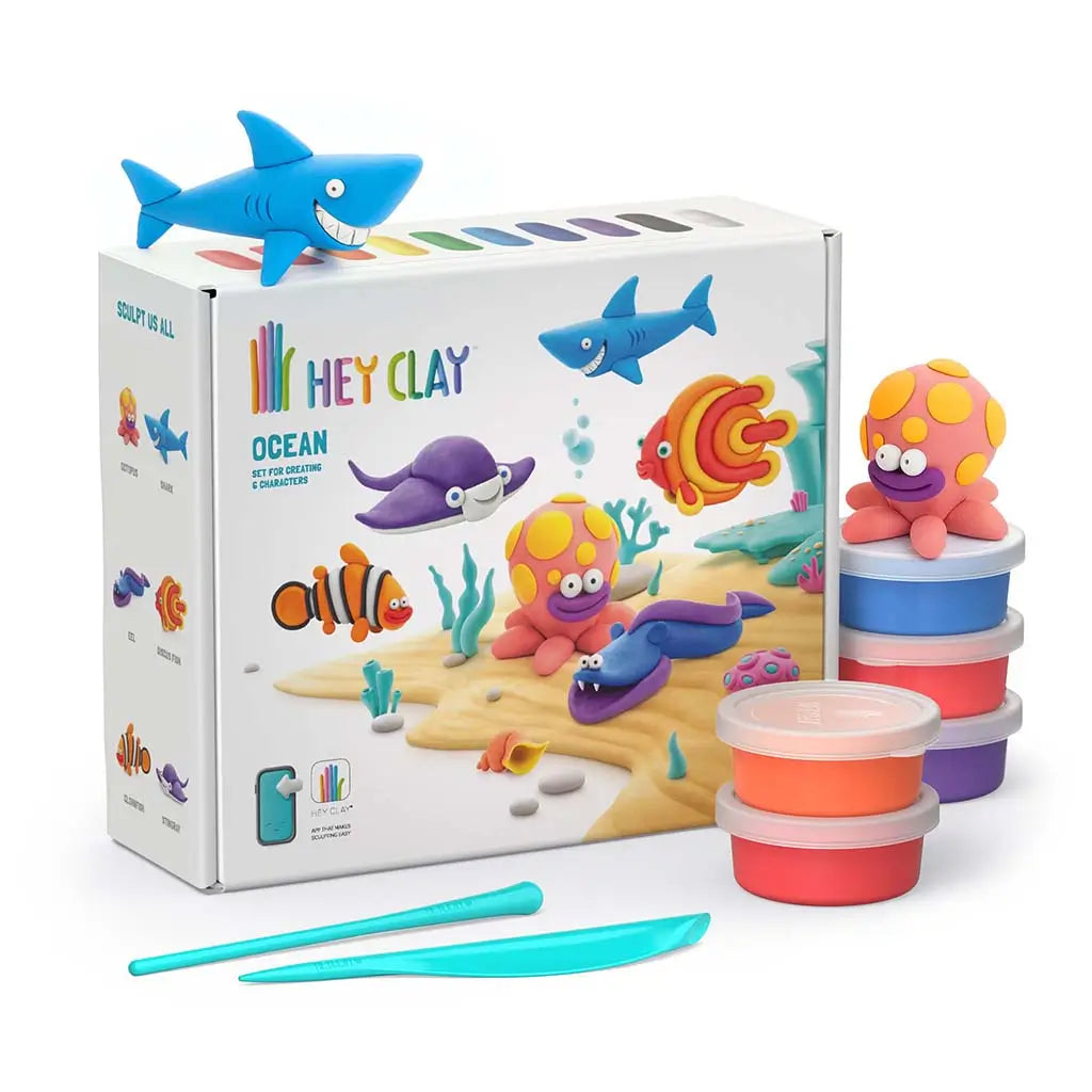 Hey Clay ocean craft kit with bright modeling clay tubs and smooth tools beside a colorful box showing rounded sea creatures on a sandy ocean scene, presented in a clean studio setting.