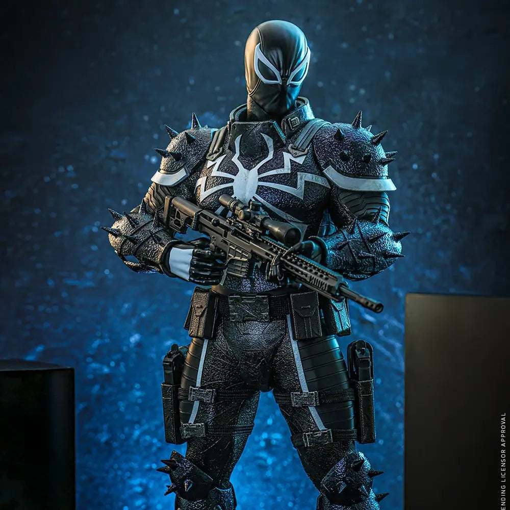 Hot Toys Agent Venom figure in black textured armor with white spider emblem and spiked shoulders, holding a scoped rifle against a dark blue studio backdrop.
