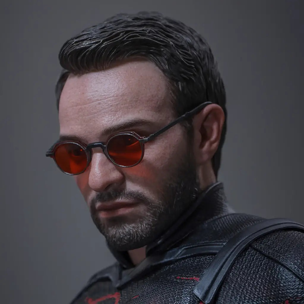 Hot Toys Marvel sixth-scale figure portrait shows a dark-haired bearded head sculpt with round red-tinted glasses and black textured costume against a plain gray backdrop.