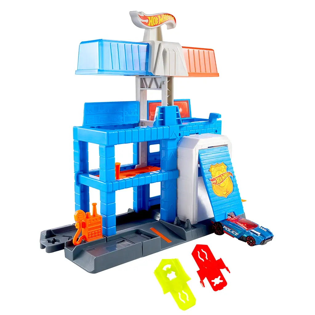 Hot Wheels City Downtown Police Tower shown from a left angle, blue molded plastic structure with orange slide ramp, opening jail door, rotating top platforms, and small police car exiting the base.