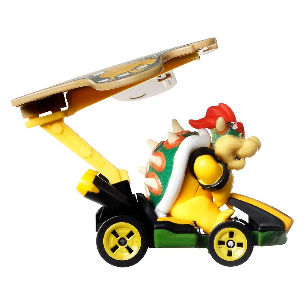 Side view of Hot Wheels Mario Kart Bowser diecast car in yellow and green with Bowser figure, spiked shell, and kite-shaped glider wing extended, displayed on white background.