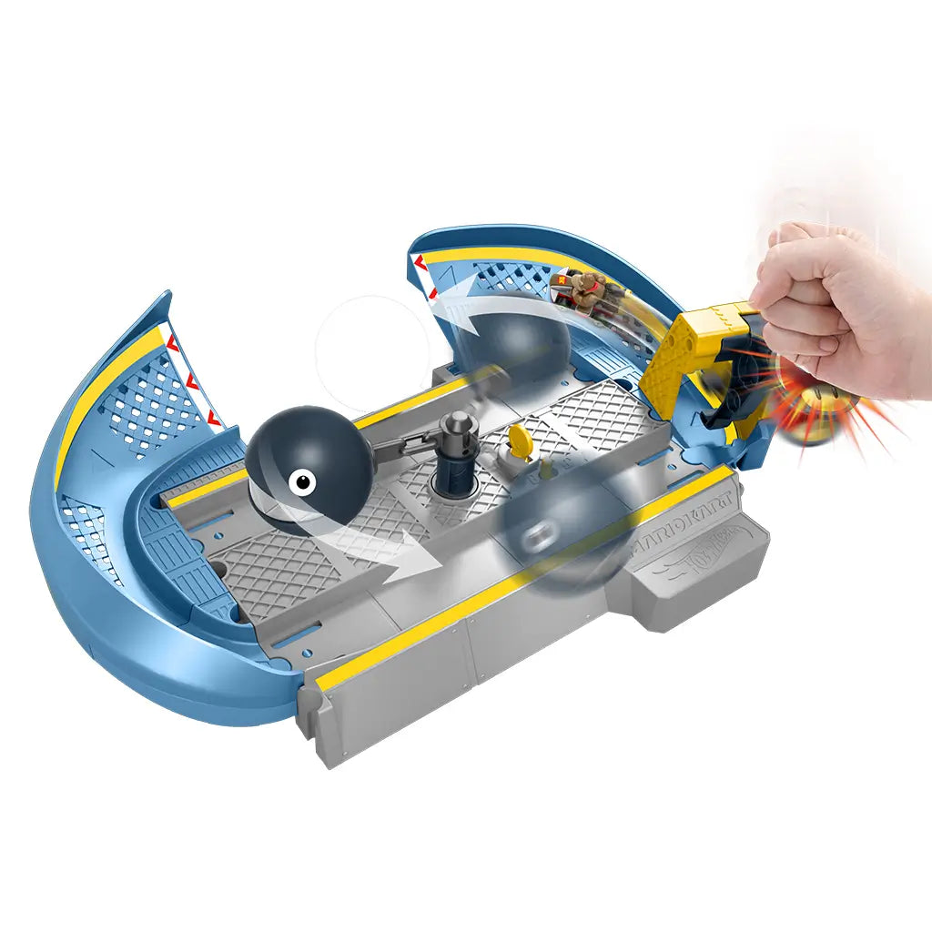 Action view of Hot Wheels Mario Kart Chain Chomp Track Set with hand pressing Mushroom Slam Launcher, propelling Donkey Kong’s kart across gray ramp past spinning Chain Chomp.