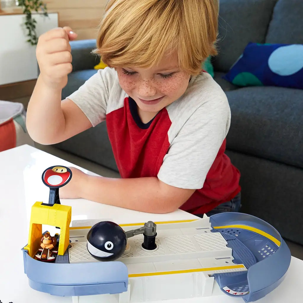 Child playing with Hot Wheels Mario Kart Chain Chomp Track Set at home, launching Donkey Kong kart with Mushroom Slam Launcher as spinning Chain Chomp obstacle moves on track.