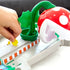 Close-up of Hot Wheels Mario Kart track showing a hand placing a yellow coin near the large red Piranha Plant with white spots and green leaves on the playset’s base.