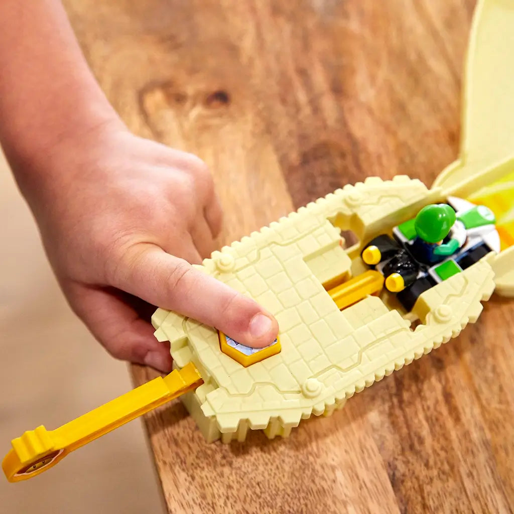 Close-up of child’s hand pressing a launcher to send Luigi’s green Hot Wheels Mario Kart speeding down the Thwomp Ruins race track, built with tan brick-style plastic details.