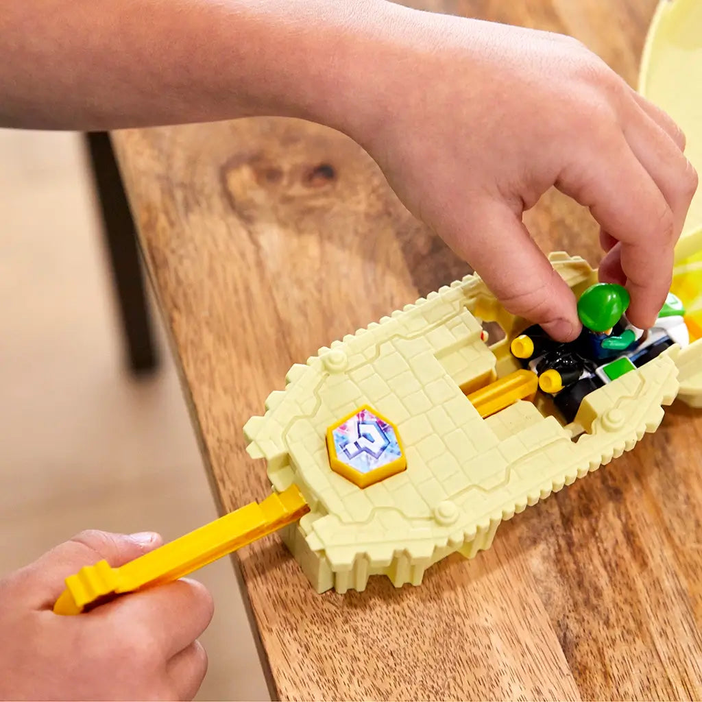 Child’s hands place Luigi’s green Mario Kart die-cast car into the tan launcher on the Hot Wheels Thwomp Ruins playset, ready to race past the smashing Thwomp block.