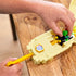 Child’s hands place Luigi’s green Mario Kart die-cast car into the tan launcher on the Hot Wheels Thwomp Ruins playset, ready to race past the smashing Thwomp block.
