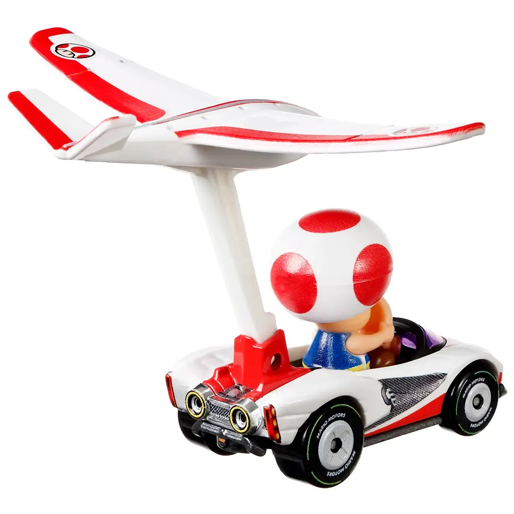 Hot Wheels Mario Kart Toad diecast car features a glossy white body with red trim, black wheels, and a raised plane glider wing in red and white attached to the rear.