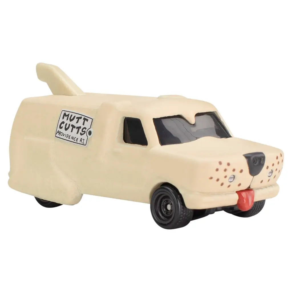 Angled front view of beige Hot Wheels Dumb and Dumber 'Mutt Cutts' van, styled like a dog with black windows, nose detail, red tongue, side logo, and tail accent on roof.