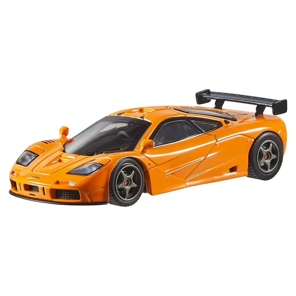 Angled view of Hot Wheels 1995 McLaren F1 GTR die-cast car in orange, highlighting sleek aerodynamic design, black spoiler, vented hood, and realistic racing details on plain backdrop.