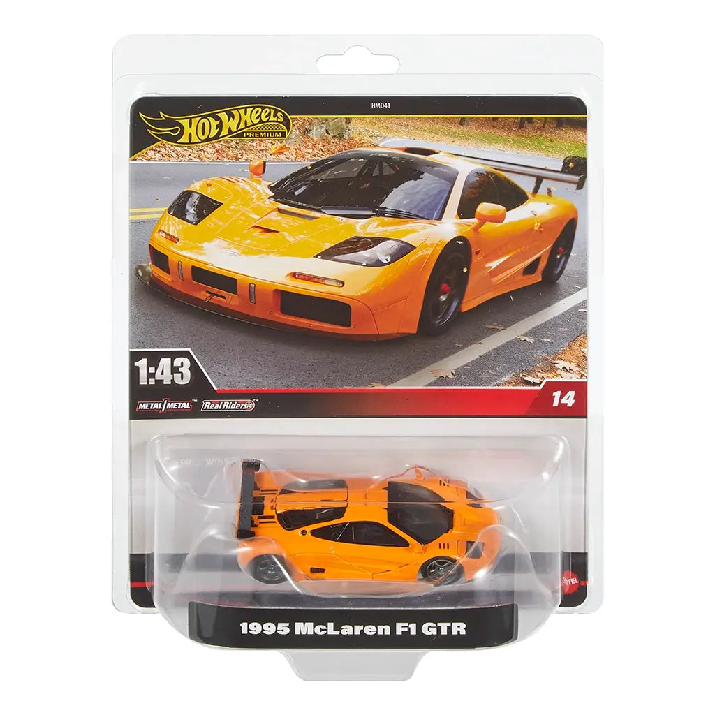 Hot Wheels Premium 1995 McLaren F1 GTR 1:43 scale die-cast car in bright orange with black accents, shown in retail packaging with street background and product branding details.