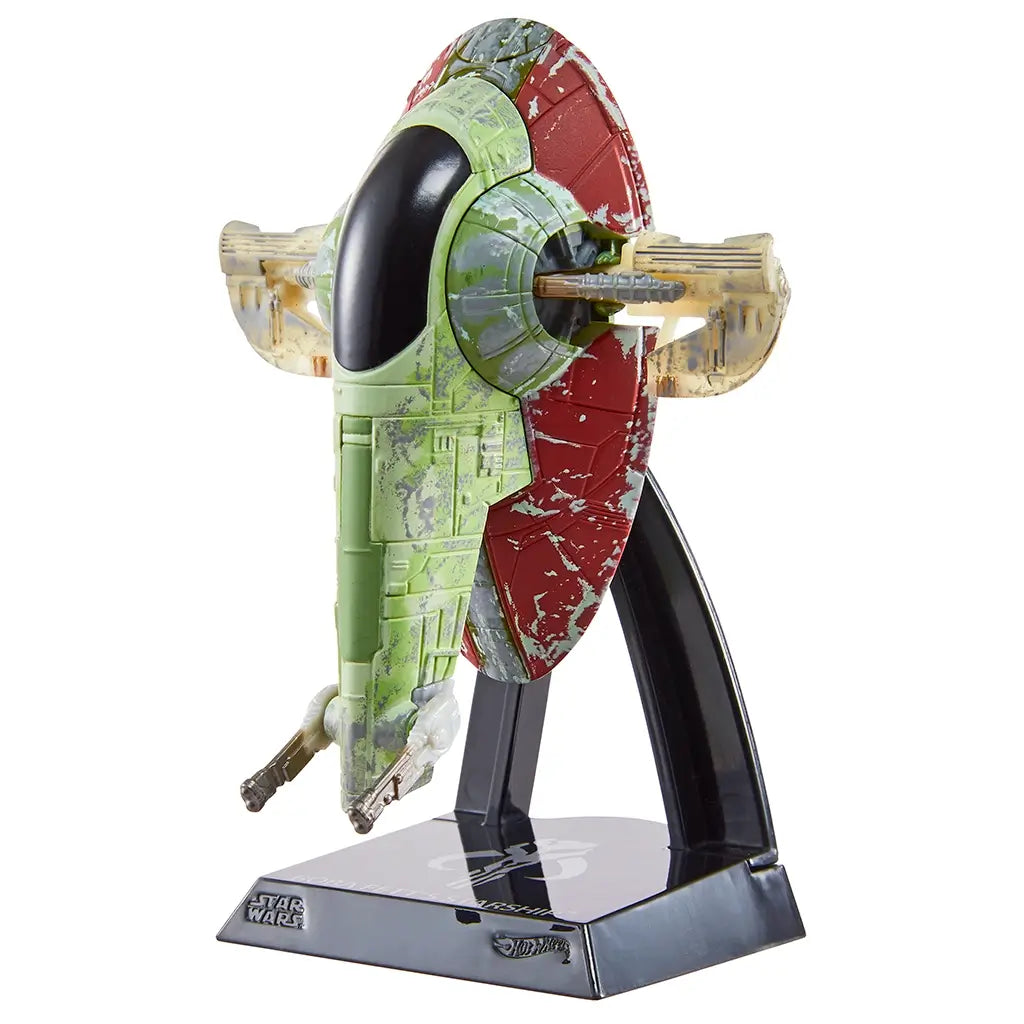 Hot Wheels Star Wars Boba Fett’s Starship shown at an angled front view with green and maroon distressed plastic finish, oval cockpit window, side-mounted cannons, and display stand highlighting the ship’s iconic vertical form.