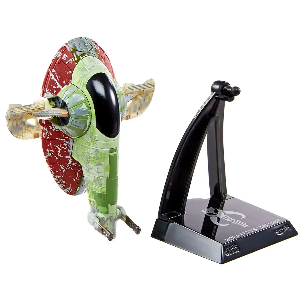 Hot Wheels Star Wars Boba Fett’s Starship collectible displayed beside its black plastic stand, showing the green and red weathered hull, compact scale size, and removable support designed for shelf display and collecting.