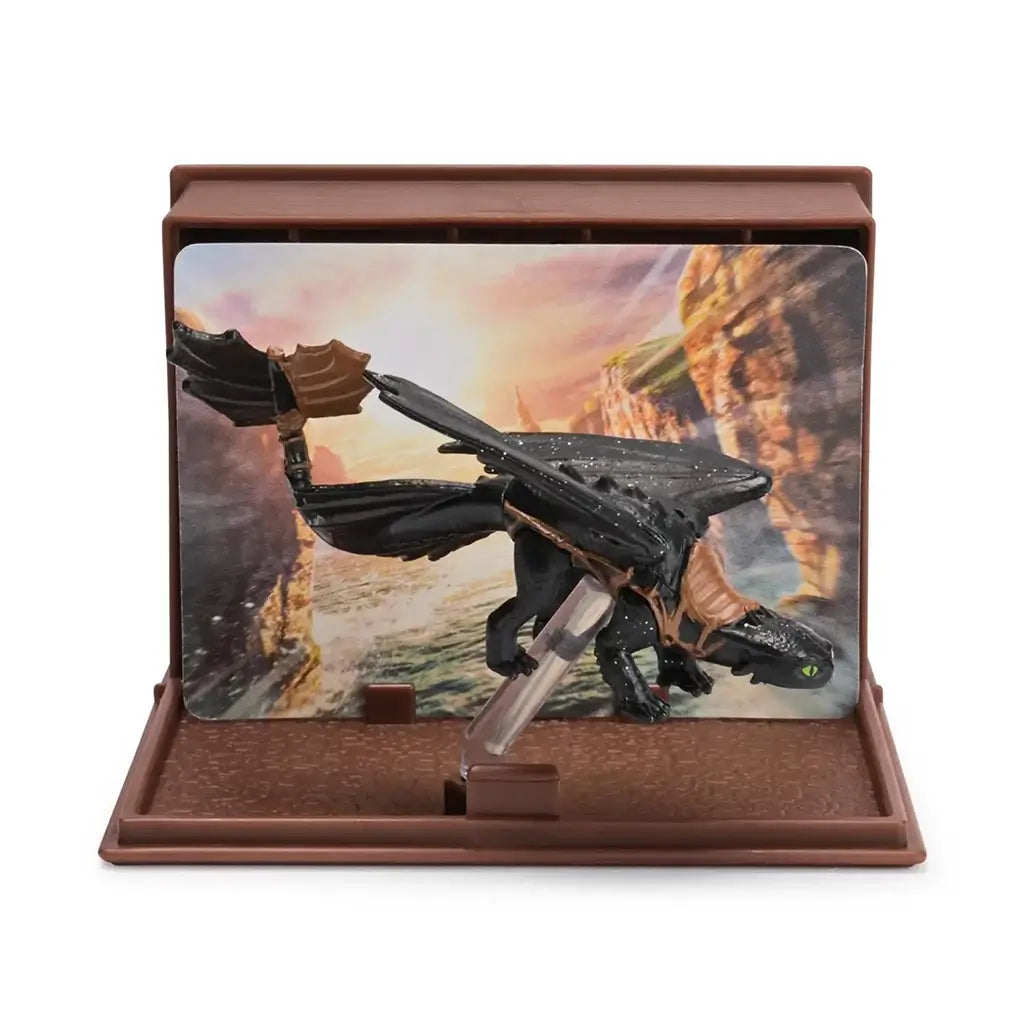 How to Train Your Dragon Toothless dragon figure in black textured plastic with wide wings and green eyes, posed on a clear stand against a scenic canyon backdrop inside a brown display case.