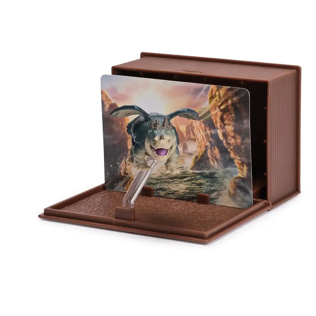 How to Train Your Dragon collectible dragon figure in green and beige plastic with wings extended in flight pose, mounted on clear stand with canyon scene backdrop inside a brown display book case.