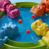 Hasbro Hungry Hungry Hippos close-up showing glossy plastic hippos in pink, orange, blue, and yellow surrounding a blue play surface with scattered red marbles ready for quick lever-press gameplay.